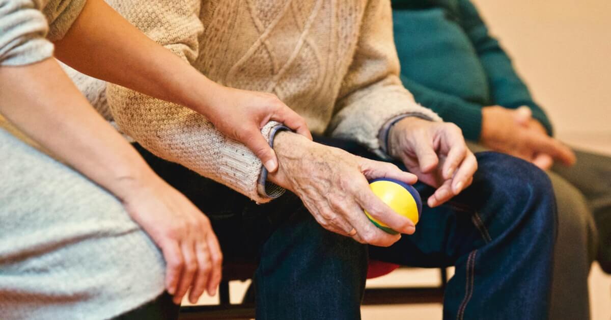 old man facing knee pain holding ball, a lady holding this old man's hand